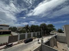 Rua em obras entre casas, com carros e mar ao fundo.